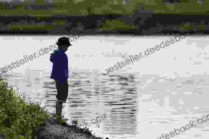 A Young Boy Stands On A Riverbank, Looking Out At The Water. The Sky Is Gray And Overcast, Reflecting The Boy's Somber Mood. In The River Jeremy Robert Johnson